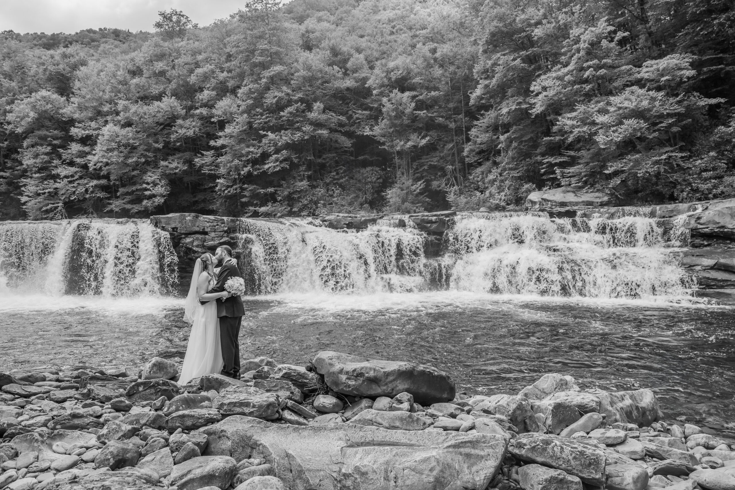 Bride and groom embracing in front of High Falls of Cheat on their Elkins West Virginia scenic train wedding excursion, photographed by Amberlee Christey Photography.